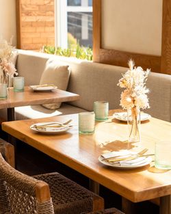 Wooden table with white plates, gold cutlery, and green glasses in a bright dining area at Casa Madera West Hollywood.
