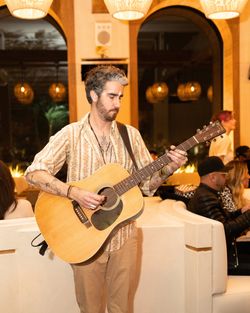 Man playing acoustic guitar inside Casa Madera West Hollywood, a live music restaurant with warm lighting and cozy seating.