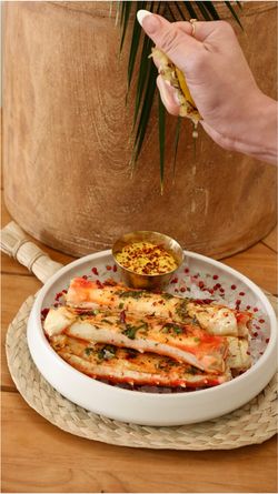 Mexican restaurant dish with seasoned seafood and a hand squeezing lime over it, accompanied by a spicy dipping sauce.