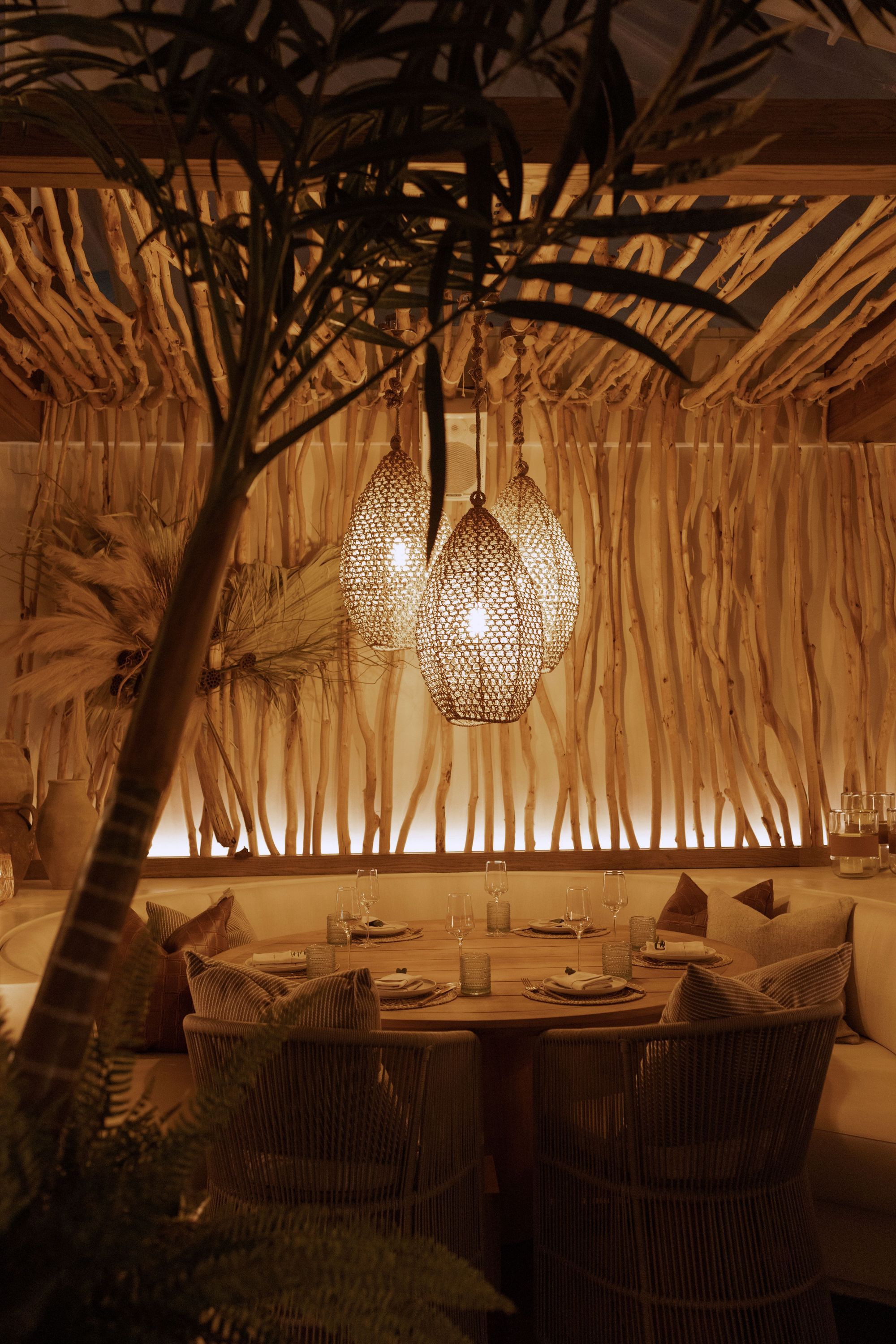 Dining area with a round wooden table, wicker chairs, and warm hanging lights at Casa Madera West Hollywood.