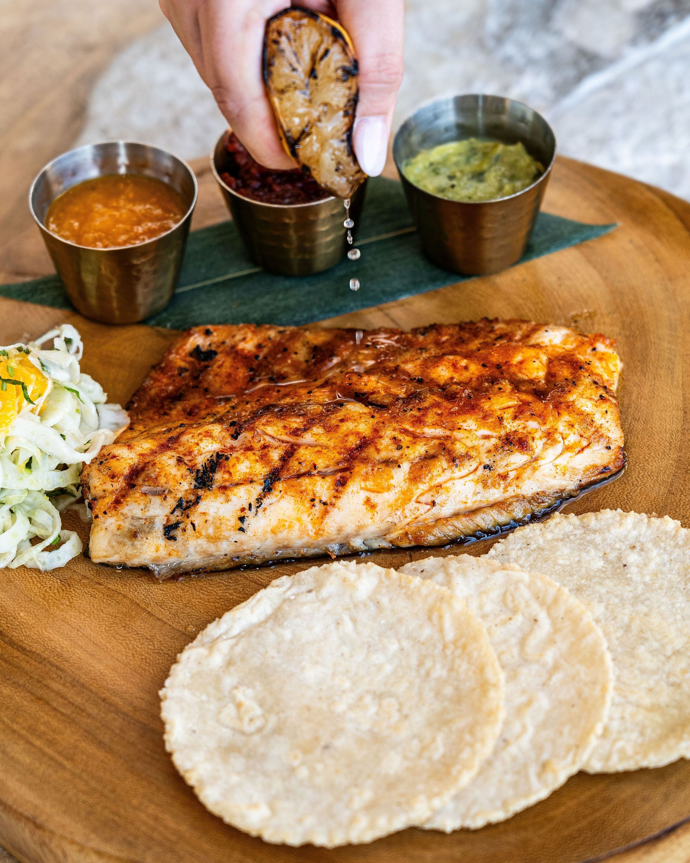 Grilled fish served with tortillas, three types of sauces, and a side of pickled vegetables at a Mexican restaurant.
